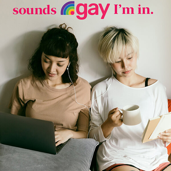 Two women relaxing in bed sharing headphones with the words 'sounds .gay I'm in.'